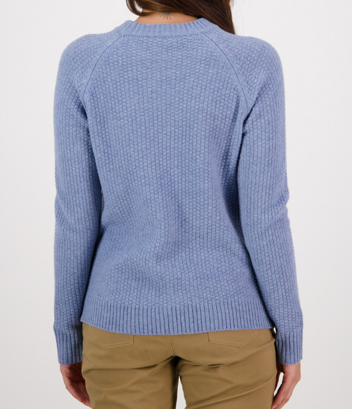 The image shows the back view of a person wearing the Swanndri Hayes Park Waffle Knit Crew, a stylish rib knit light blue sweater, and beige pants. The person has long brown hair, and the background is plain white.