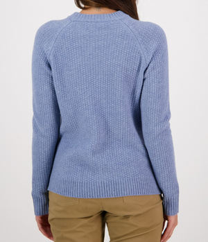 The image shows the back view of a person wearing the Swanndri Hayes Park Waffle Knit Crew, a stylish rib knit light blue sweater, and beige pants. The person has long brown hair, and the background is plain white.