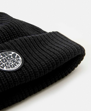 Close-up of a Rip Curl Icons Reg Beanie in black, featuring a fleece lining and a small circular patch with stylized textured writing. Set against a light, neutral background.