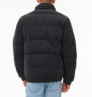 A person wearing a black Rip Curl Rincon Cord Puffer Jacket with padded lining and light blue jeans stands facing away, displaying the back of the jacket against a plain white background.