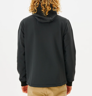 A person with curly blonde hair wears a black Rip Curl Anti Series Soft Tech Fleece Jacket, celebrated for its wind resistance, paired with beige pants, standing back to the camera against a plain white background.