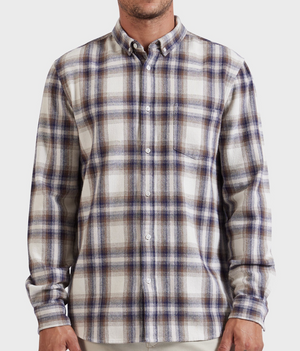 A person is wearing the Academy Brand Colorado Shirt, a long-sleeved, button-up shirt with a white, brown, and blue plaid pattern. The stylish garment is made from 100% cotton and features a front pocket on the left side along with buttoned cuffs. The person's face is not visible.