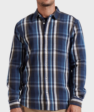 A man wears the Academy Brand So Cal Shirt, a 100% cotton plaid long-sleeve button-up in blue, white, and brown, while standing against a plain light gray background. His face is partially out of frame.