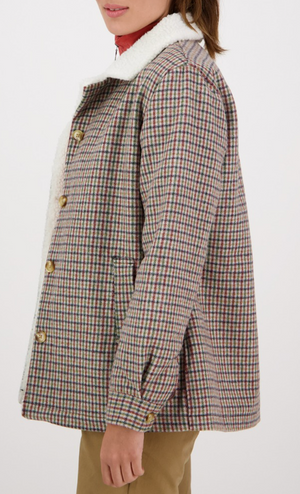 A person wearing a Swanndri Capitola Sherpa Jacket with a plaid pattern and white fleece collar, paired with tan pants, is shown from the side against a plain background with their face partially out of view.