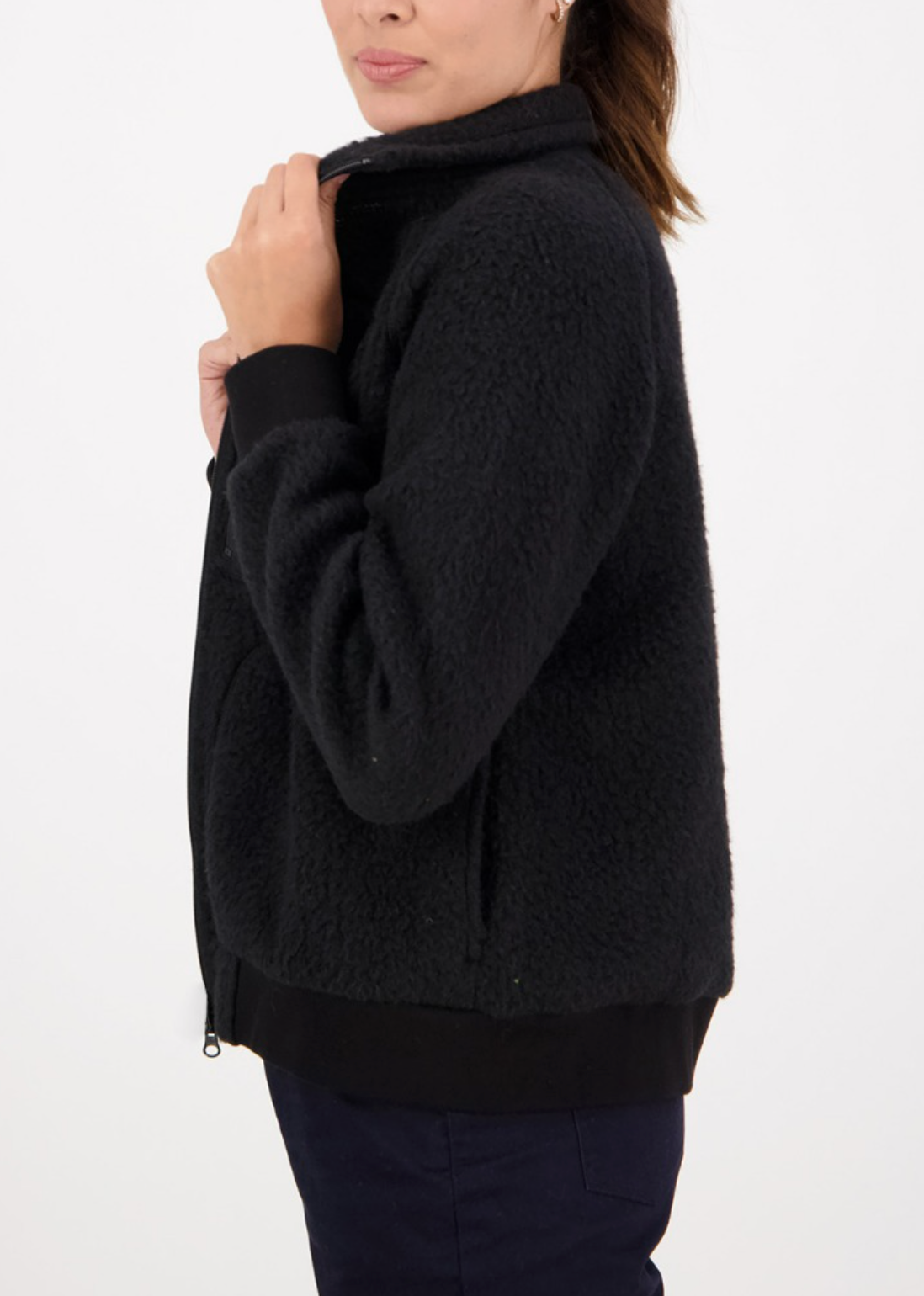 A person is wearing a Swanndri Newgate wool fleece jacket in black, standing sideways against a plain white background. They hold the collar with one hand, highlighting the cozy texture of the jacket.