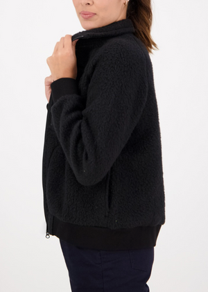 A person is wearing a Swanndri Newgate wool fleece jacket in black, standing sideways against a plain white background. They hold the collar with one hand, highlighting the cozy texture of the jacket.