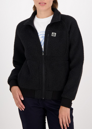 A person is wearing a cozy Swanndri Newgate Wool Fleece Jacket in black, featuring a high collar, zip closure, and an embroidered chest patch over a white shirt. Paired with dark pants against a plain white background.