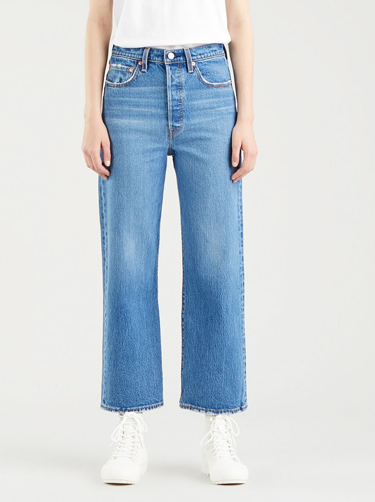 A person wearing Levis Ribcage Straight Jeans in light blue and a white shirt is styled with white lace-up ankle boots, standing against a plain white background.