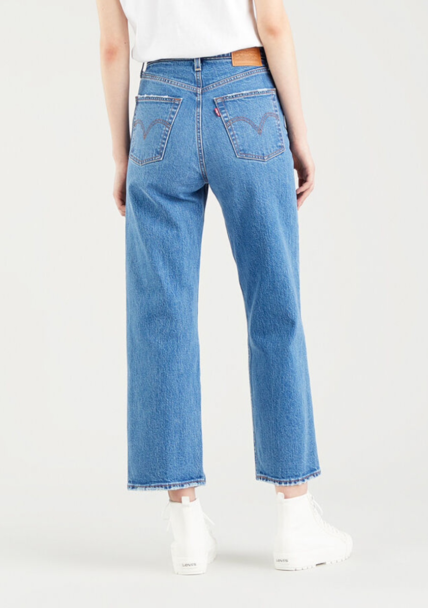 A person is seen from behind in Levis Ribcage Straight Jeans with blue high waist and arcuate-stitched back pockets, highlighting the slim fit. They're paired with a white top and high-top sneakers against a light background.