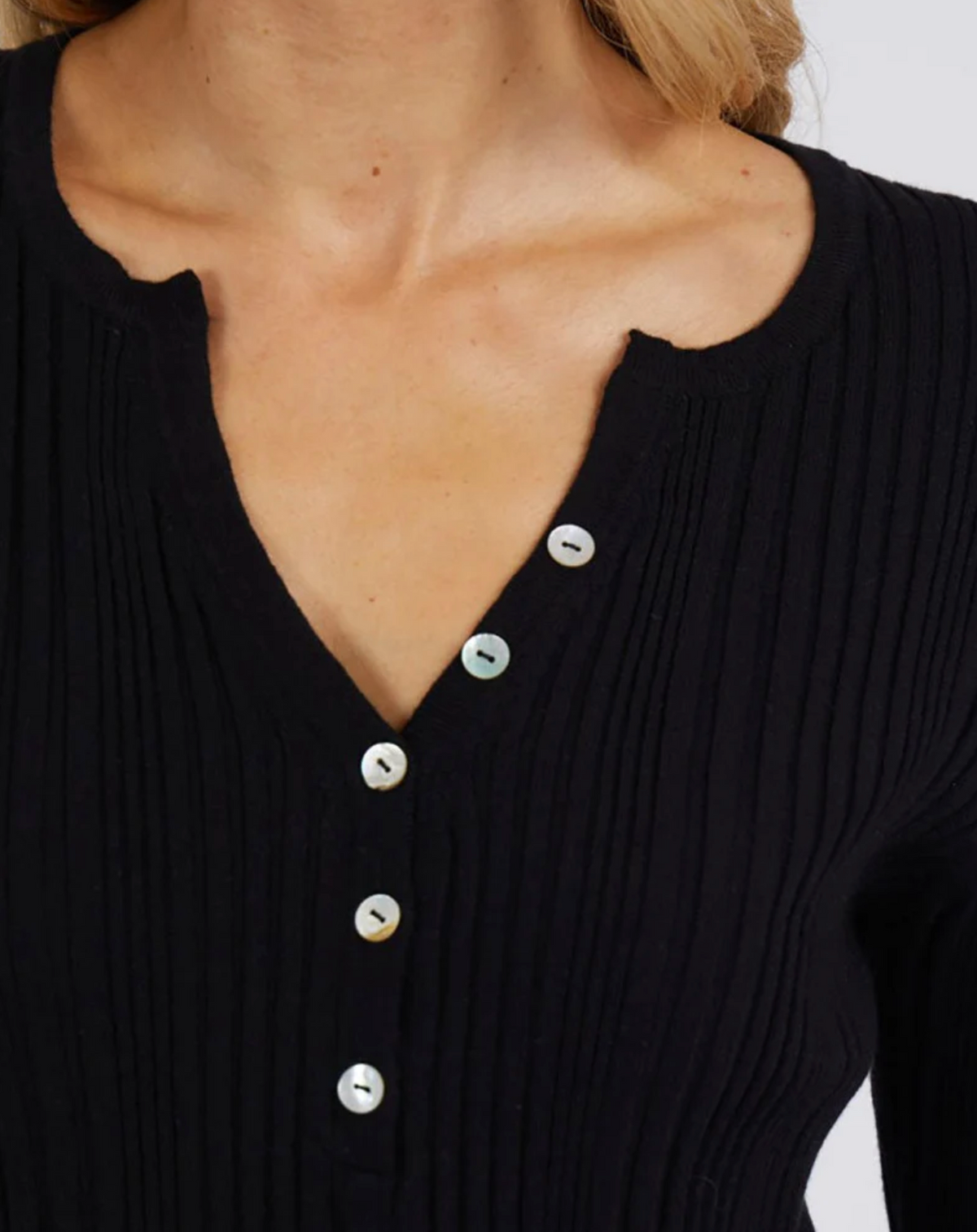 A close-up of a person wearing the Foxwood Hannah Rib Knit, a black top featuring a vee neckline with a notch and five white buttons down the front.