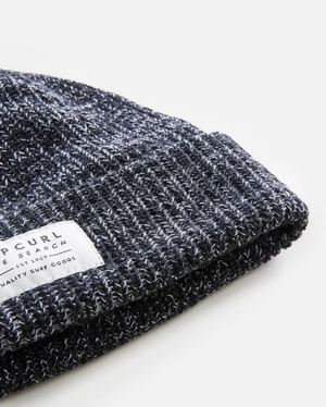 A close-up of the gray Rip Curl Dusk Fleece Lined Regular Beanie, neatly folded with a white fabric tag displaying small printed text, set against a plain white background.