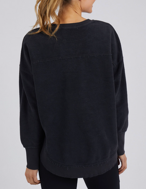 A person with blond hair is seen from the back wearing a Foxwood Cozy Simplified Crew teddy fleece sweater featuring the subtle Foxwood logo, paired with black pants against a plain light gray background.