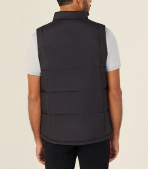 A man is seen from the back wearing the NNT Puffer Vest, a black high neck quilted vest with lightweight 3M Thinsulate, over a light gray short-sleeve shirt and black pants, standing against a plain light background.