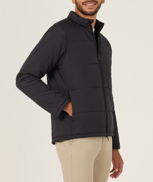 A man wearing the NNT Puffer Jacket in black, featuring 3M Thinsulate, and beige pants stands smiling with one hand in his pocket against a plain light background.