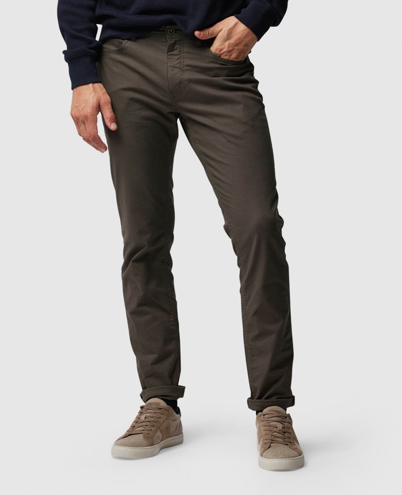 A person is standing and wearing a pair of Rodd & Gunn straight fit jeans, a dark sweater, and beige sneakers. The photo is cropped above the waist, and the background is a plain light gray.