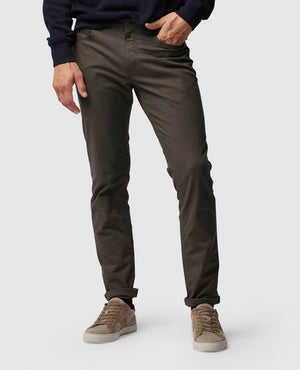 A person is standing and wearing a pair of Rodd & Gunn straight fit jeans, a dark sweater, and beige sneakers. The photo is cropped above the waist, and the background is a plain light gray.