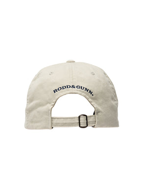 The image shows the back view of the Rodd & Gunn Signature Cap, a beige cotton twill baseball cap with an adjustable strap. The brand name "RODD & GUNN" is embroidered above the strap in navy blue letters, marking it as a standout piece from the stylish brand.