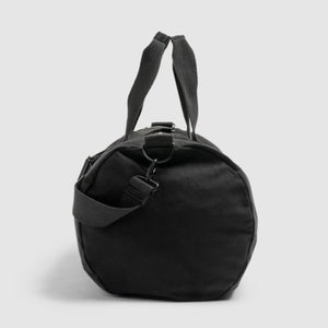 The Rodd & Gunn Richmond Road Duffle Bag is a black cylindrical duffle crafted from durable cotton canvas, featuring short handles and an adjustable shoulder strap, standing upright against a light gray background. It seamlessly blends functionality with style.