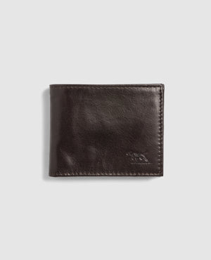 The Rodd & Gunn Leeston Dunsandel Road Wallet is a closed dark brown Buffalo Leather wallet, featuring a subtly embossed animal logo on the bottom right corner against a light gray backdrop. It boasts a smooth, slightly shiny texture with card slots and a coin pocket for practicality.