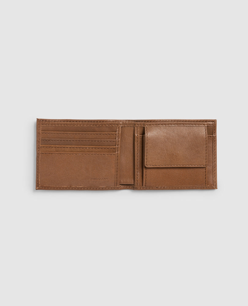The Rodd & Gunn Leeston Dunsandel Road Wallet, made of brown buffalo leather, sits open on a gray background. It features multiple card slots on the left and a convenient flap-covered coin pocket on the right, with interior stitching enhancing the smooth leather texture.