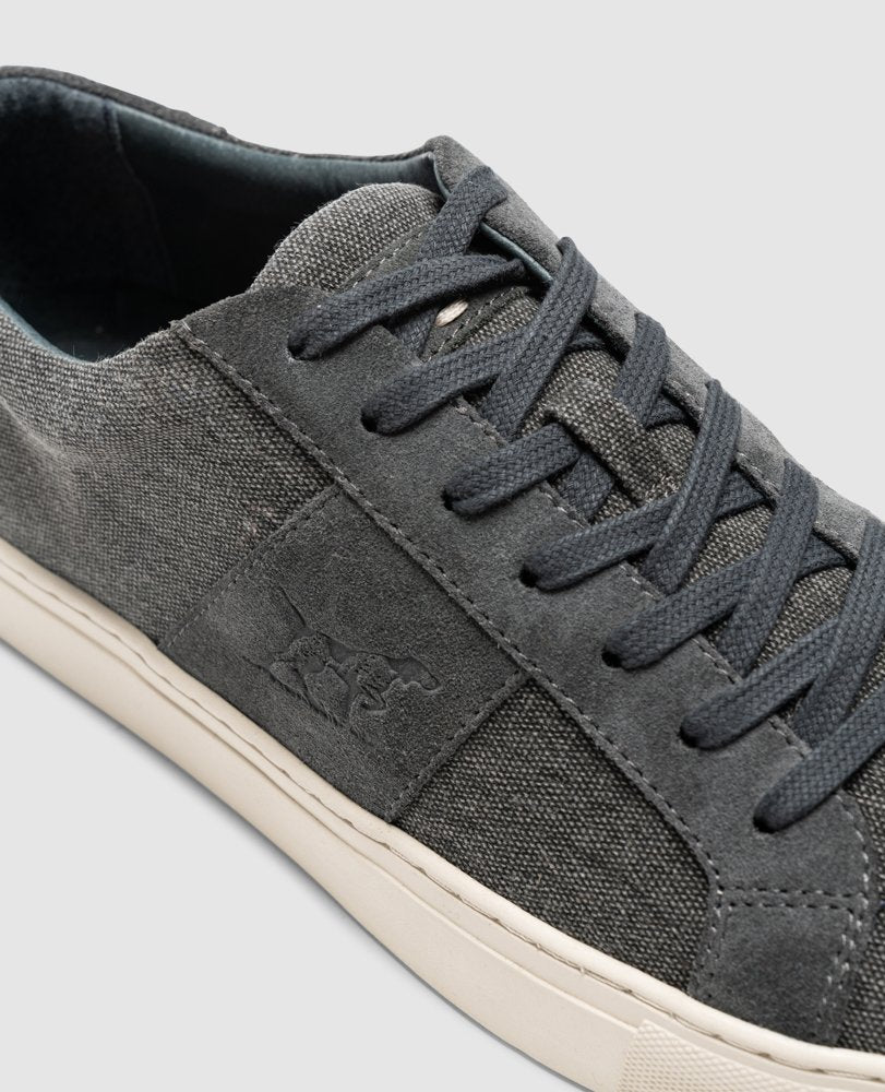 Close-up of the Rodd & Gunn Endeavour Sail Sneaker in gray, featuring dark gray laces and a white sole. The sneaker has a subtle embossed logo on the side panel and is crafted from suede and canvas with suede leather trims for added style. The background is light gray.