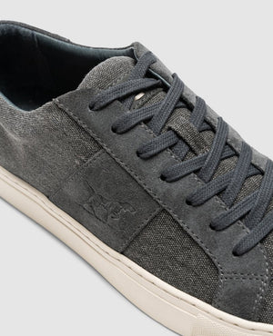 Close-up of the Rodd & Gunn Endeavour Sail Sneaker in gray, featuring dark gray laces and a white sole. The sneaker has a subtle embossed logo on the side panel and is crafted from suede and canvas with suede leather trims for added style. The background is light gray.