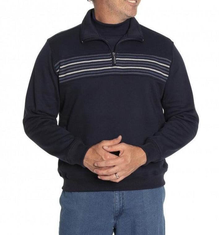 A person wearing the Breakaway Narcise Snowy Mt Fleece, a dark navy blue half-zip fleece with horizontal stripes across the chest and sleeves. The individual is also wearing blue jeans and stands with their hands clasped together, looking slightly to the side.