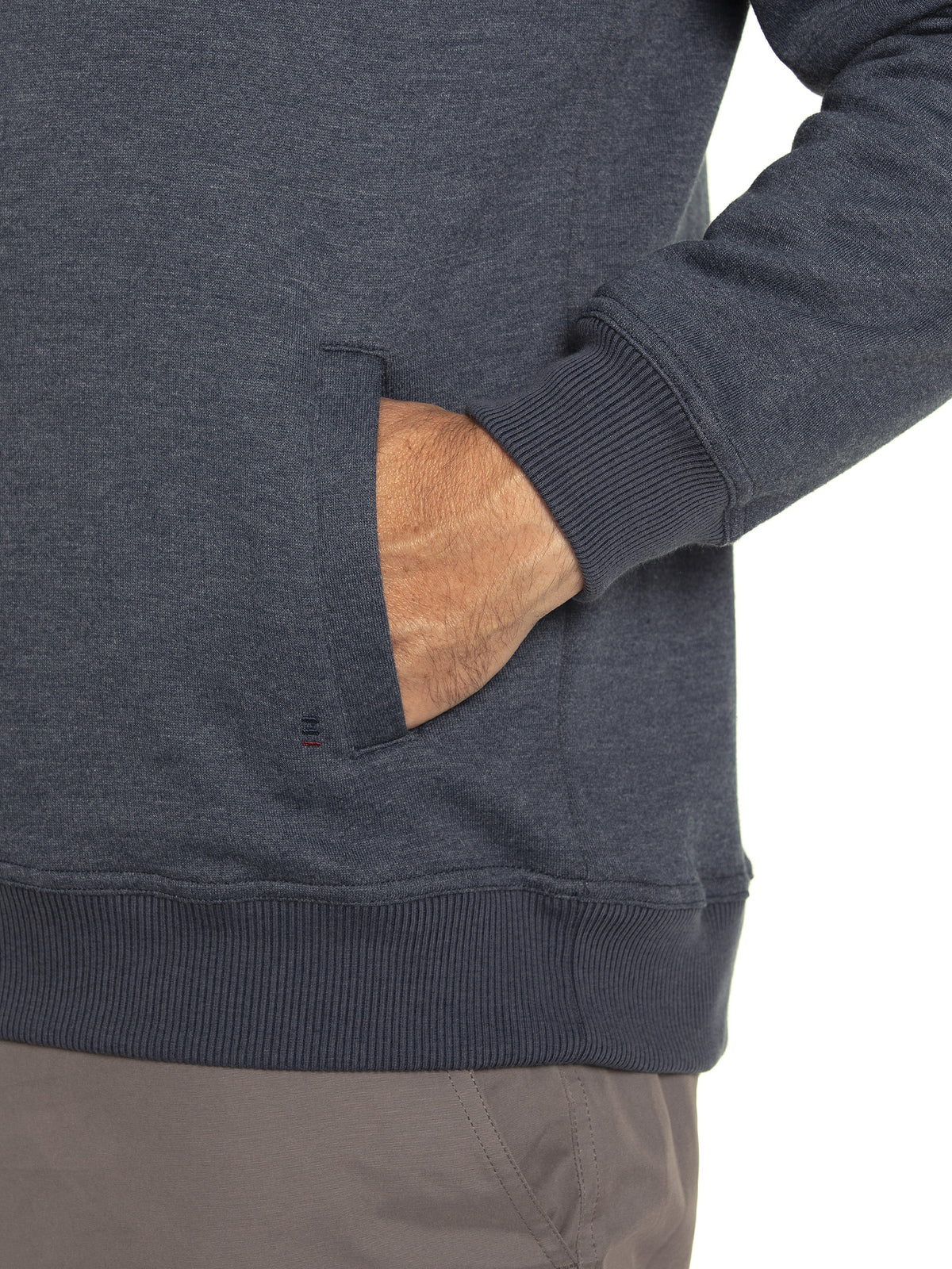 Someone wears the Breakaway Zed Snowy Mt Fleece Half Zip in dark gray as a pullover with ribbed cuffs, their right hand in the pocket. Paired with light gray pants, this cozy fleece-lined outfit contrasts beautifully against the plain white background.