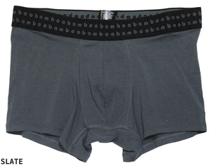 The Bamboo Trunks are gray men's boxer briefs with a black waistband, featuring a repeating "bam" logo in light gray. Made from soft bamboo fabric, these comfortable trunks offer anti-bacterial properties to ensure all-day freshness. The color of the boxer briefs is labeled as "SLATE" in the bottom left corner.