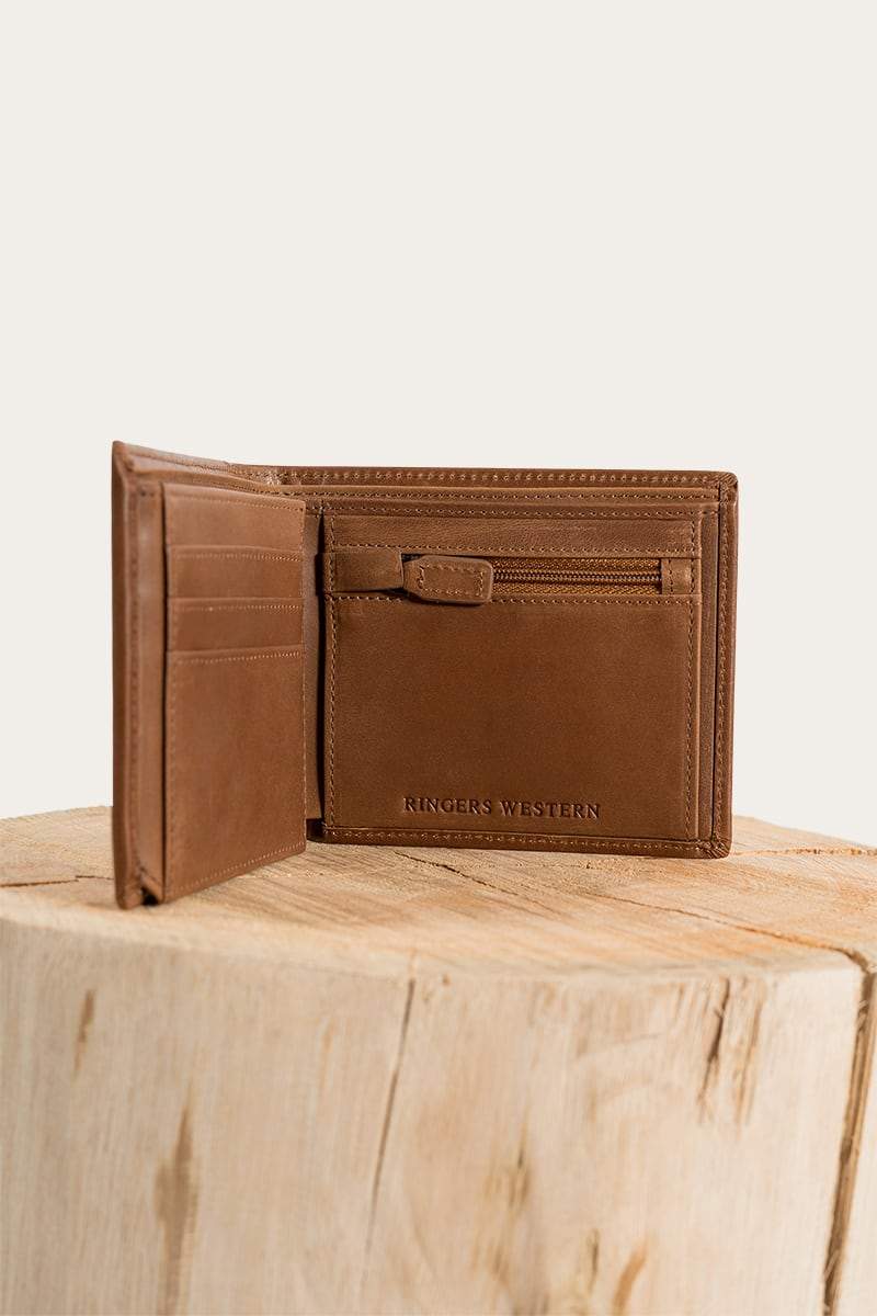 The Ringers Western Bayview Wallet, made of genuine leather, has multiple card slots and a spacious compartment. Displayed on a wooden surface, it features the embossed brand name inside.