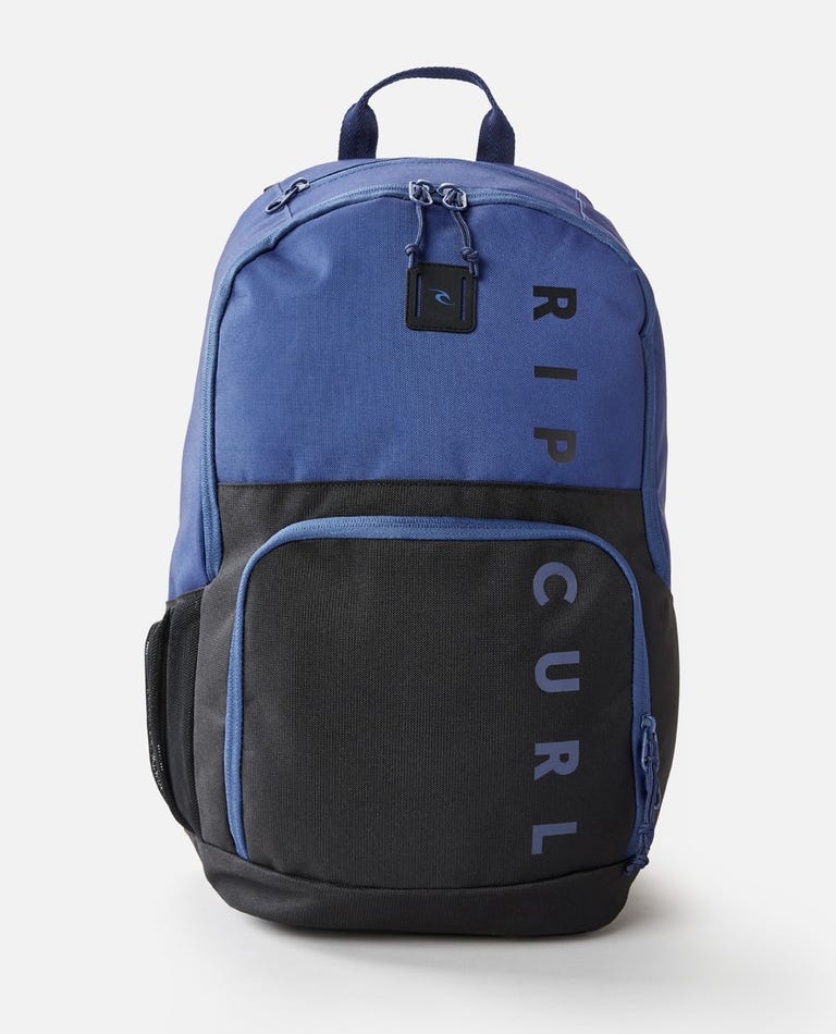 The Rip Curl Evo 24L Hope Eco Backpack in blue and black features a top handle, zippered main compartment, front pocket, and cooler compartment. "RIP CURL" is boldly printed vertically in black on the blue section against a white backdrop.