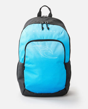 The Rip Curl Ozone 30L School Eco Backpack is crafted from recycled plastic and boasts a blue and black design with a front zipper pocket. The front pocket showcases a stylized white wave graphic, and the brand name "RIP CURL" is printed above it in white letters. It also includes a laptop compartment, carrying handle, and two zippers.