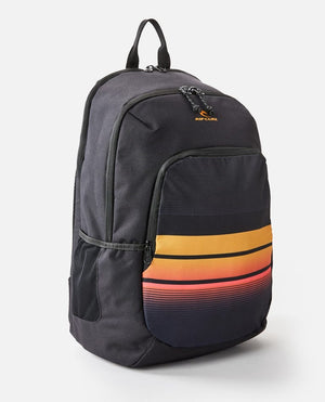 The Rip Curl Ozone 30L School Eco Backpack, made from recycled plastic, sports a black design with vibrant orange, pink, and yellow gradient stripes on the front pocket. It has two zippered compartments, a laptop compartment, top handle, and side mesh pockets for essentials.