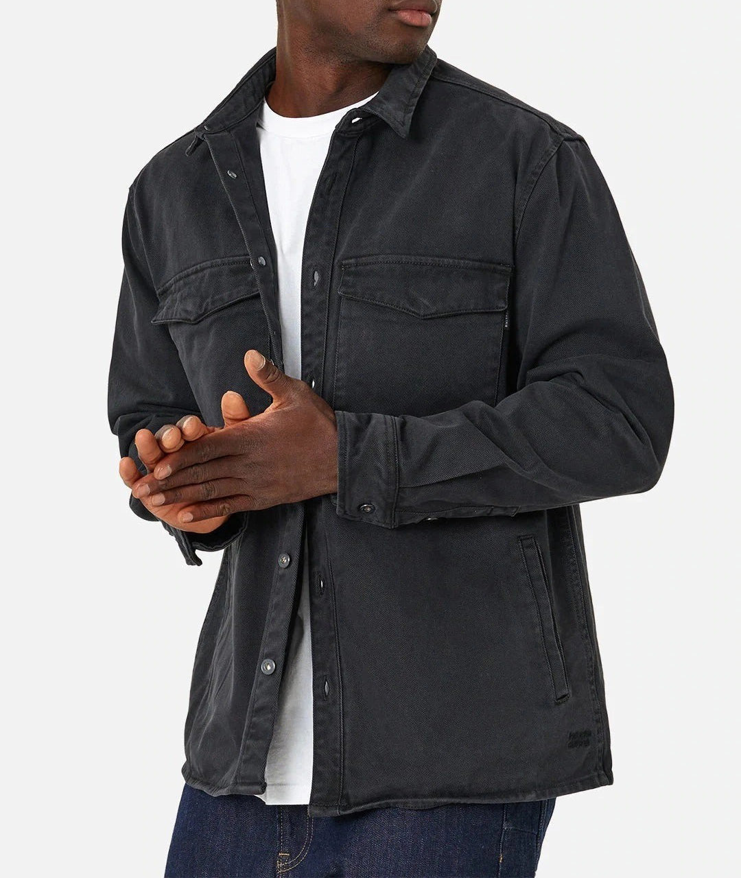 A person stands against a plain background, hands clasped, wearing Industrie The Woodbury Shirt in dark gray over a white t-shirt and blue jeans. The comfortable cotton jacket resembles a stylish shirt with two breast pockets.