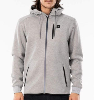 A person wearing a light gray Rip Curl Anti Series Departed Zip Thru hoodie with a small black logo on the upper left side. The winter clothing features two front zippered pockets, a drawstring hood, and Durable Water Resistant (DWR) fabric. The person is standing against a plain white background.