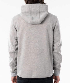 A person with long hair is pictured from behind, wearing a light gray Rip Curl Anti Series Departed Zip Thru hooded sweatshirt and dark pants. The hood of the sweatshirt is up, highlighting its winter clothing features. This outfit exemplifies the Rip Curl Anti Series' commitment to both style and functionality in adverse weather conditions.