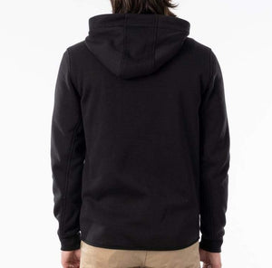 A person with long, dark hair is shown from behind, wearing the Rip Curl Anti Series Departed Zip Thru hoodie in black paired with tan pants. This winter-appropriate hoodie sets a stylish tone against the plain white backdrop.
