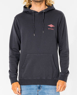 Someone is wearing a black Rip Curl Quality Products Hood made from a cotton/polyester blend, featuring a small chest logo and a front pocket. It's paired with light blue jeans, enhancing their curly hair against the plain background for a stylish look.