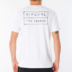 A person with light-colored hair is seen from the back, wearing a comfortable Rip Curl 50/50 Scratch Tee. The white T-shirt, crafted from 100% cotton, boasts a rectangular design featuring "RIP CURL" at the top and "THE SEARCH" underneath in a hand-drawn style inside the rectangle.