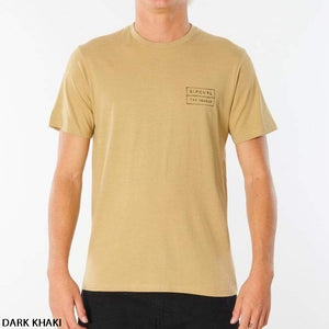 A person wearing the Rip Curl 50/50 Scratch Tee, a short-sleeve, dark khaki 100% cotton shirt with "RIP CURL THE SEARCH" text printed on the left chest. The comfortable tee is paired with black pants against a plain white background.