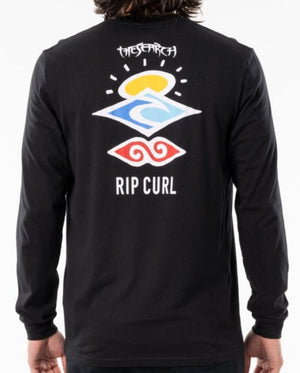 A person wearing a Rip Curl Search Icon Long Sleeve Tee in black. The organic cotton shirt's back features colorful abstract shapes with "THE SEARCH" above and "RIP CURL" below.