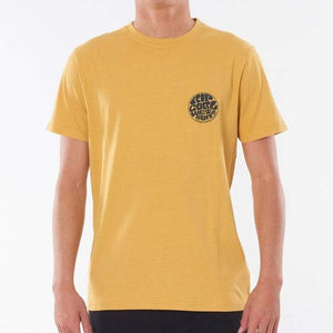 A person wearing the Rip Curl Wetsuit Icon Tee, a plain yellow T-shirt featuring a small circular Rip Curl print logo on the upper left side of the chest. The logo displays stylized text that is somewhat difficult to read. This comfortable tee, made from 100% cotton, sets off against a plain white background.