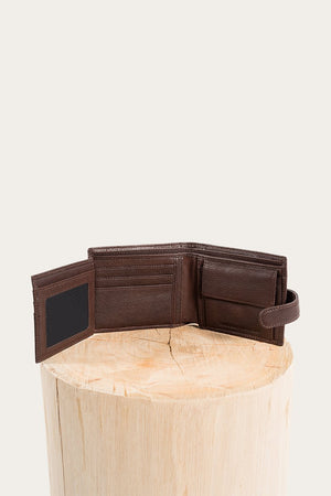 The Ringers Western Cypress Wallet, made of genuine leather, is unfolded to show multiple card slots and a compartment, positioned on a light wooden stump against a simple pale backdrop.