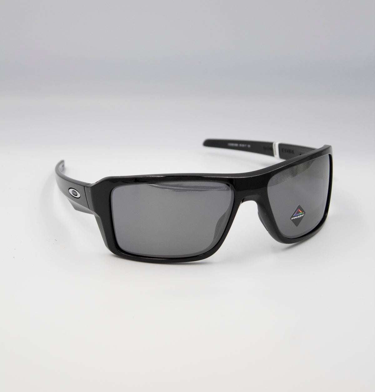 The Oakley Double Edge Polarized sunglasses exude timeless style with sleek black rectangular frames, a semi-matte finish, and polarised lenses that offer UV protection. A small diamond-shaped logo adorns the right lens. Photographed on a plain white background, they embody functionality.