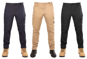 Three pairs of UNIT Demolition Stretch Cargo Pants are displayed on mannequins. From left to right, the colors are navy blue, khaki, and black. All pants feature cargo-style pockets and buttons at the waist. The mannequins are wearing beige work boots. Each durable work pant has a small logo tag on the thigh.