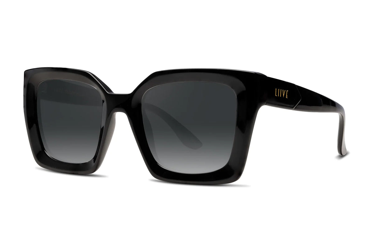The Liive Desire Sunglasses feature a pair of black, oversized rectangular frames with dark tinted polycarbonate lenses and glossy arms bearing the Liive brand name in gold. These chic sunglasses provide stylish UV protection and are elegantly positioned on a white background.