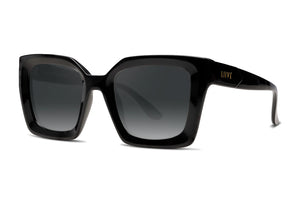 The Liive Desire Sunglasses feature a pair of black, oversized rectangular frames with dark tinted polycarbonate lenses and glossy arms bearing the Liive brand name in gold. These chic sunglasses provide stylish UV protection and are elegantly positioned on a white background.