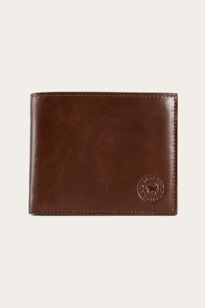 The Ringers Western Duke Wallet is a brown leather accessory showcasing a smooth surface with visible stitching along the edges. The wallet features a circular embossed logo in the lower right corner and exemplifies genuine craftsmanship, being made from high-quality leather.