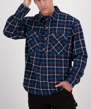 A person is wearing a shirt from the Swanndri Egmont Flannelette Twin Pack, featuring a blue plaid design with white and black stripes. The comfortable, long sleeve brushed cotton shirt is buttoned down the front and has two chest pockets. Casually running a hand through their hair, they place the other hand in a pocket.
