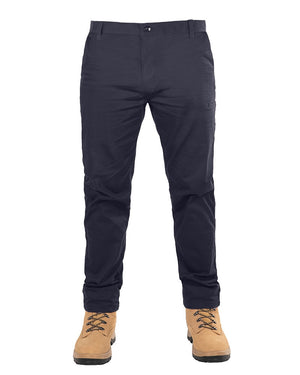 A person is wearing dark blue UNIT Ignition Stretch Pants and tan work boots. The image captures the lower body from the waist down, showcasing the snug-fitting stretch fabric of the pants and the laced-up boots with sturdy soles.